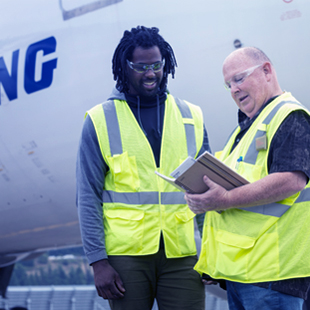 Two people in safety vests and protective eye wear looking at a book