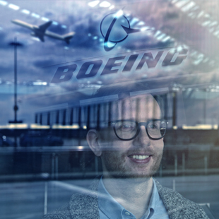 Person with glasses looking out of a window with the reflection of the Boeing logo reflected